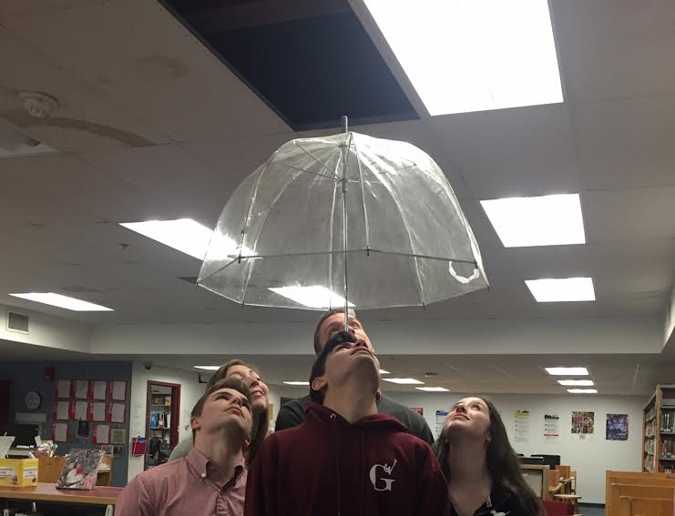 Students pose with umbrella under  the latest leak in the library