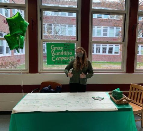 Junior Kyia Karvelas at lunch with green bandanas to give away and a poster for students.